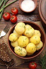 Tasty young boiled potatoes with dill in bowl served on wooden table, flat lay