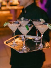 Waiter serves elegant cocktails on a silver tray at a vibrant evening event indoors