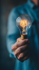 Person's hand holding a lit Edison-style light bulb, signifying a new idea or concept graphic design