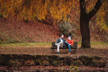 Son and older father sitting on bench by lake and talking.