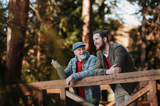 Older father and his son standing on bridge, looking at nature.