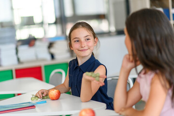 Schoolgirl in canteen eating fruit during snack break.