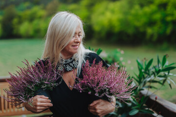 Mature woman standing by potted heathers on terrace.