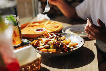 Plate with fries and vegetables served on wooden table in restaurant. Closeup of fresh food with sauce and drink. Tasty dinner detail. Casual dining lifestyle concept.