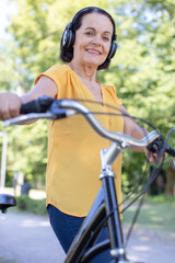 Obraz premium senior woman wearing earphones riding city bike in town