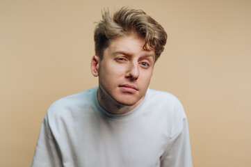 Fototapeta premium Young man expresses uncertainty with a squint against a neutral background in a casual setting