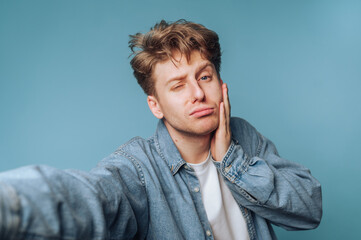 Young man making a funny face while posing for a selfie against a blue background in a casual setting