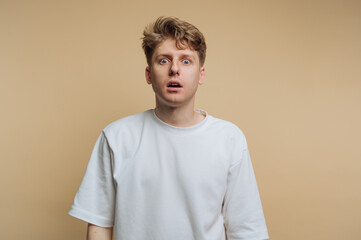 Surprised young man expressing disbelief against a neutral background during an unexpected moment