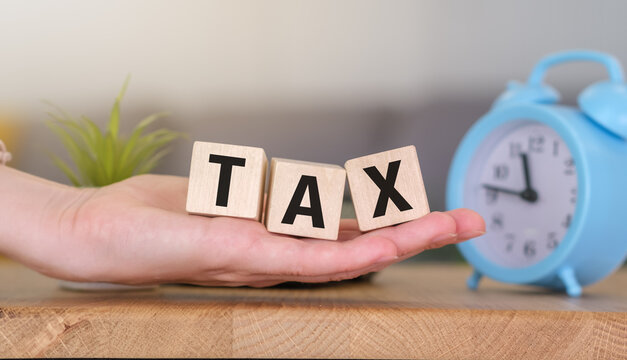 Hand holding wooden cubes of text TAX on the table. Business Concept