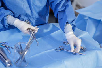 Gloved hands arranging sterile surgical instruments on blue drape