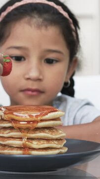 Vertical video: Hand reaching in with strawberry and placing it atop pancakes to crown breakfast
