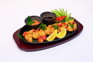 Traditional Japanese gyoza on a traditional plate, garnished with cucumber and vegetables, served on a palm leaf with sauces.