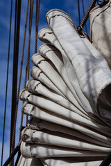 Classic boat folded sail. Lines of ropes against blue sky. Textures and shapes of vintage sailing environment. Sense of adventure, nostalgia, maritime tradition.