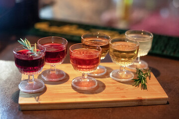 A selection of colorful cocktails served in vintage glassware on a wooden tray, garnished with sprigs of rosemary, creating a cozy and inviting atmosphere