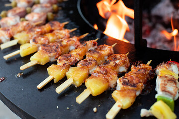 Mini skewers of pineapple and shrimp grilling over an open flame.