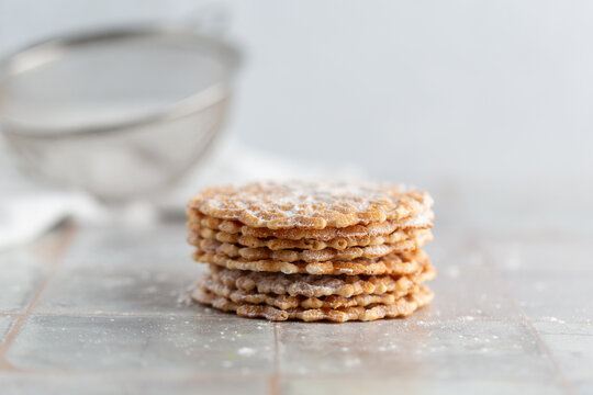 Pizzelles sprinkled with Powdered Sugar stacked on a white tile kitchen counter
