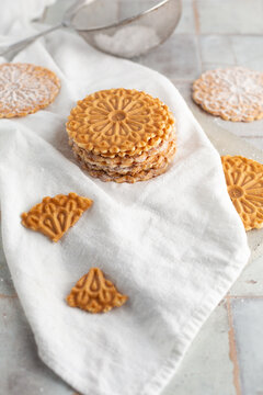 Pizzelles sprinkled with Powdered Sugar stacked on a white tile kitchen counter