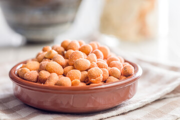 Peanuts in a crispy crust in bowl on checkered napkin.