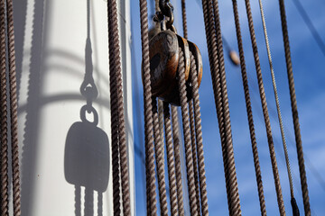 Sailing ship rigging ropes and wooden pulley block casting shadow on mast. Nautical detail and maritime craftsmanship. Exploration, tradition, voyage concepts.