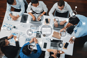 A dynamic office scene capturing a team engaged in a collaborative meeting, utilizing laptops and charts to analyze data and strategize on digital marketing initiatives. Amity