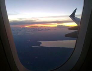 Airplane window view of sunset over land and water