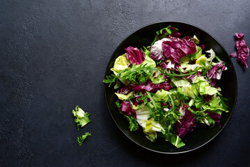 Mix of fresh salad leaves on a black plate. Top view with copy space.