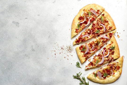Tart flambe ( tarte flambee ) - onion pie with soft cheese and smoked bakon on alight slate, stone or concrete background. Top view  with copy space.