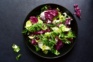 Mix of fresh salad leaves on a black plate. Top view with copy space.