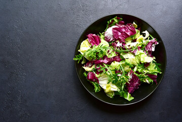 Mix of fresh salad leaves on a black plate. Top view with copy space.