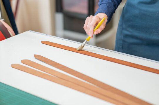 A craftsman uses a brush to cover leather parts. 