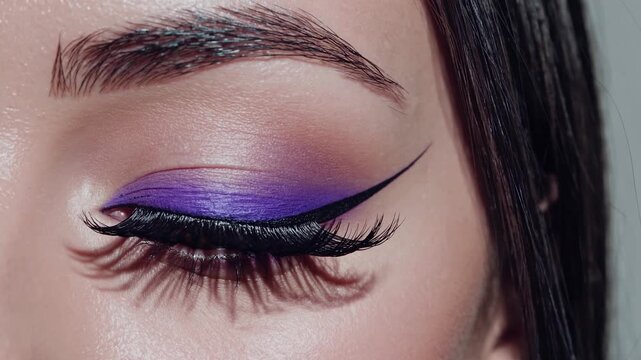 Professional makeup artist applying vivid purple eyeshadow and sharp black eyeliner, crafting glamorous dramatic makeup on closed eye