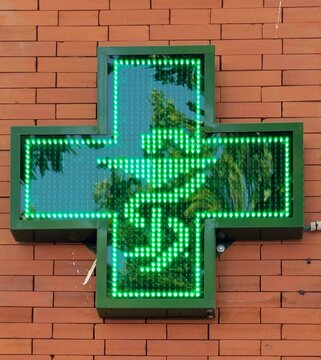 Cruz verde de farmacia con silueta de serpiente con c&aacute;liz, en muro de ladrillos 