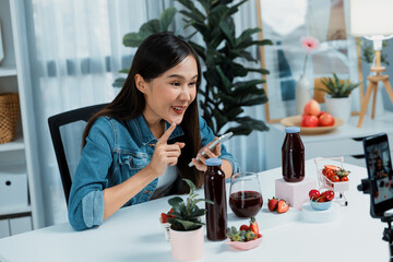 Smiling young beautiful Asian reviewing tasty mixed strawberry and cherry juice detox drinks,...