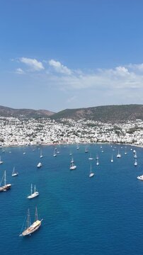 Aerial view of yachts and boats in blue sea with Greek white houses in the background
