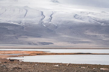 Panorama landscape of Lake Karakul in the Pamir mountains in the Tien Shan against the background of high snowy rocky peaks with clouds, morning panorama of the lake for the background