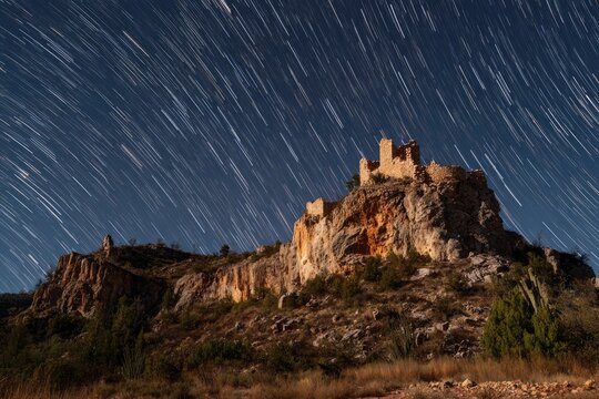Star trails over a rocky hilltop castle