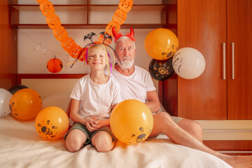 Happy child with grandfather holds balloons on Halloween night The orange balloons sparkle in the decorated room while the grandfather and child enjoy the Halloween night