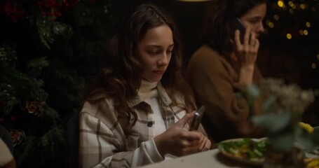 A brunette teenage girl sits and scrolls social networks on her phone during a family dinner at the table