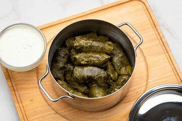 Stuffed grape leaves called dolma in steel pot with yogurt sauce on wooden board