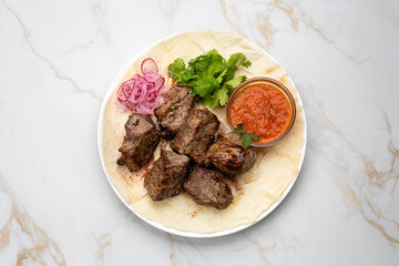 Traditional Georgian grilled meat (mtsvadi) with onion, herbs, and sauce on lavash