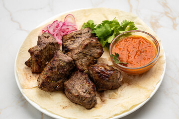 Traditional Georgian grilled meat (mtsvadi) with onion, herbs, and sauce on lavash