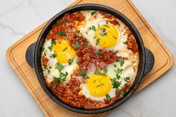 Shakshuka in cast iron skillet with tomatoes, herbs, and sunny-side-up eggs