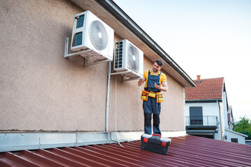 Technician installing air conditioning units using smartphone on a roof