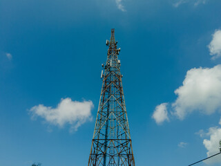 Obraz premium Tall communication tower against a bright blue sky with scattered clouds, symbolizing technology, connection, and modern infrastructure. 