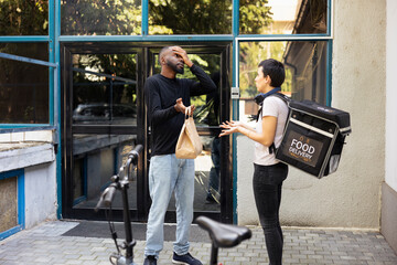Confused black man checks delivery bag with the wrong meal order, a shipping problem. A takeaway...