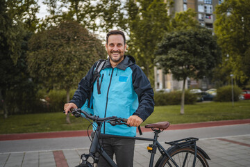 Obraz premium Smiling delivery man holding his bicycle in a city park
