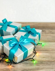Silver gift boxes with teal ribbons, Christmas lights on wooden table