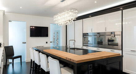 Modern kitchen interior featuring a black island with a wooden countertop and a crystal chandelier providing elegant lighting for a luxurious home