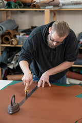 Leatherworker measuring and cutting leather in workshop. 