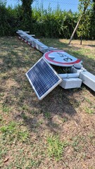 A solar-powered road barrier and a sign lie on the ground, damaged and out of service. The scene highlights vandalism, broken infrastructure, and the impact on public safety and transport systems.